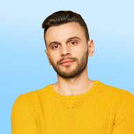 Portrait of a man with short dark hair and a trimmed beard, wearing a yellow sweater against a light blue background.