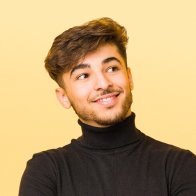 Smiling young man with short brown hair wearing a black turtleneck looking to the side against a yellow background.