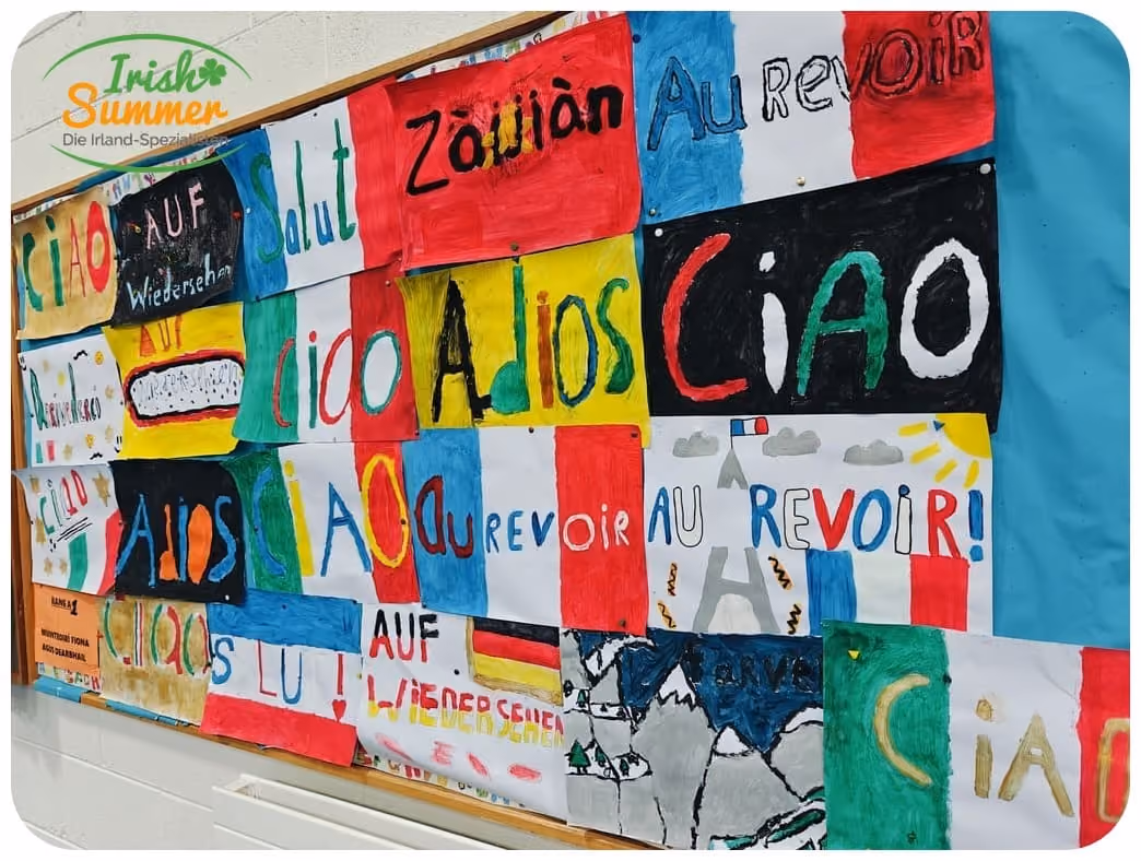 Bunte Wand mit handgemalten Willkommens- und Abschiedsgrüßen in verschiedenen Sprachen, darunter Ciao, Au Revoir und Adios.