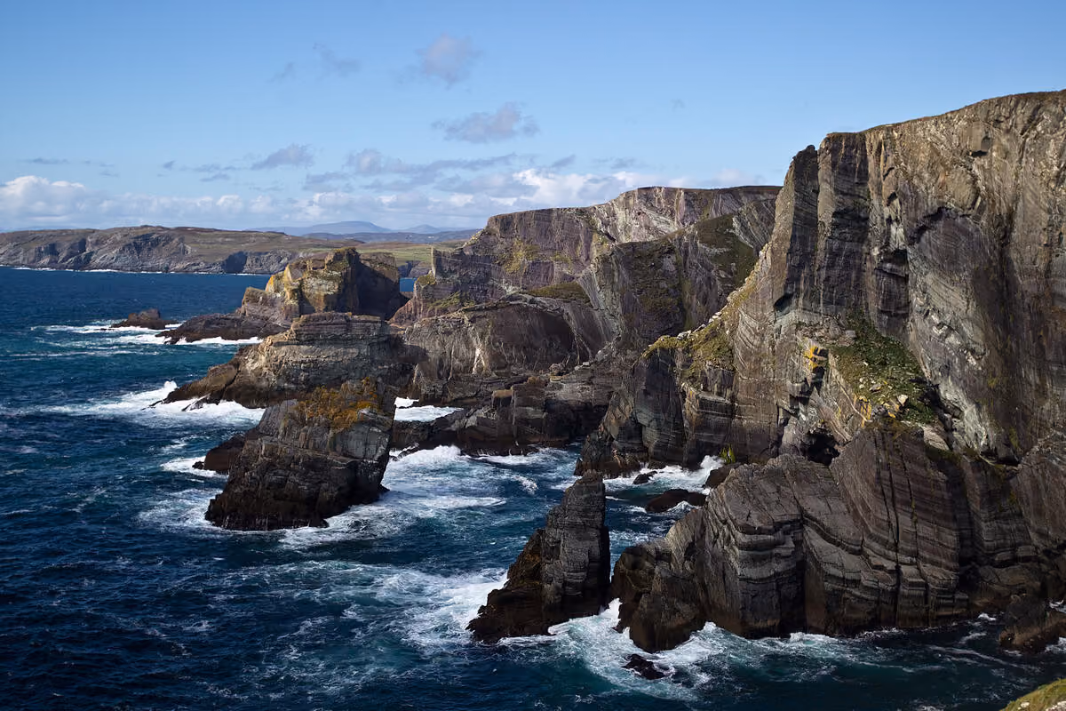 Küstenklippen mit rauschenden Wellen unter einem blauen Himmel an der Mizen Head in County Cork, Irland.