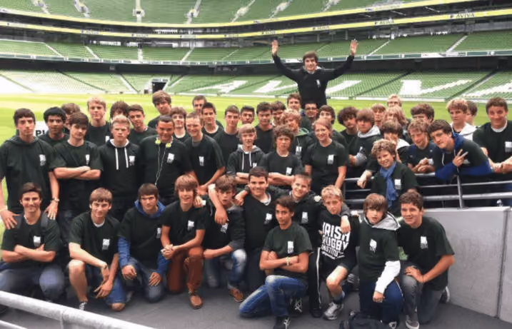 Große Gruppe von Jugendlichen in grünen T-Shirts posiert vor den Tribünen eines großen Rugby-Stadions.