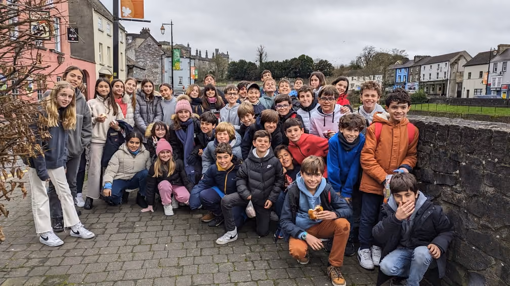 Große Gruppe von Kindern und Jugendlichen posiert auf einem gepflasterten Gehweg in einer Stadt bei bewölktem Himmel.