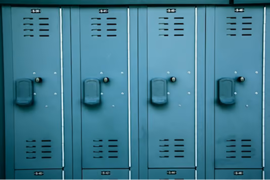 A row of teal metal lockers with vents and built-in handles, aligned side by side against a wall.