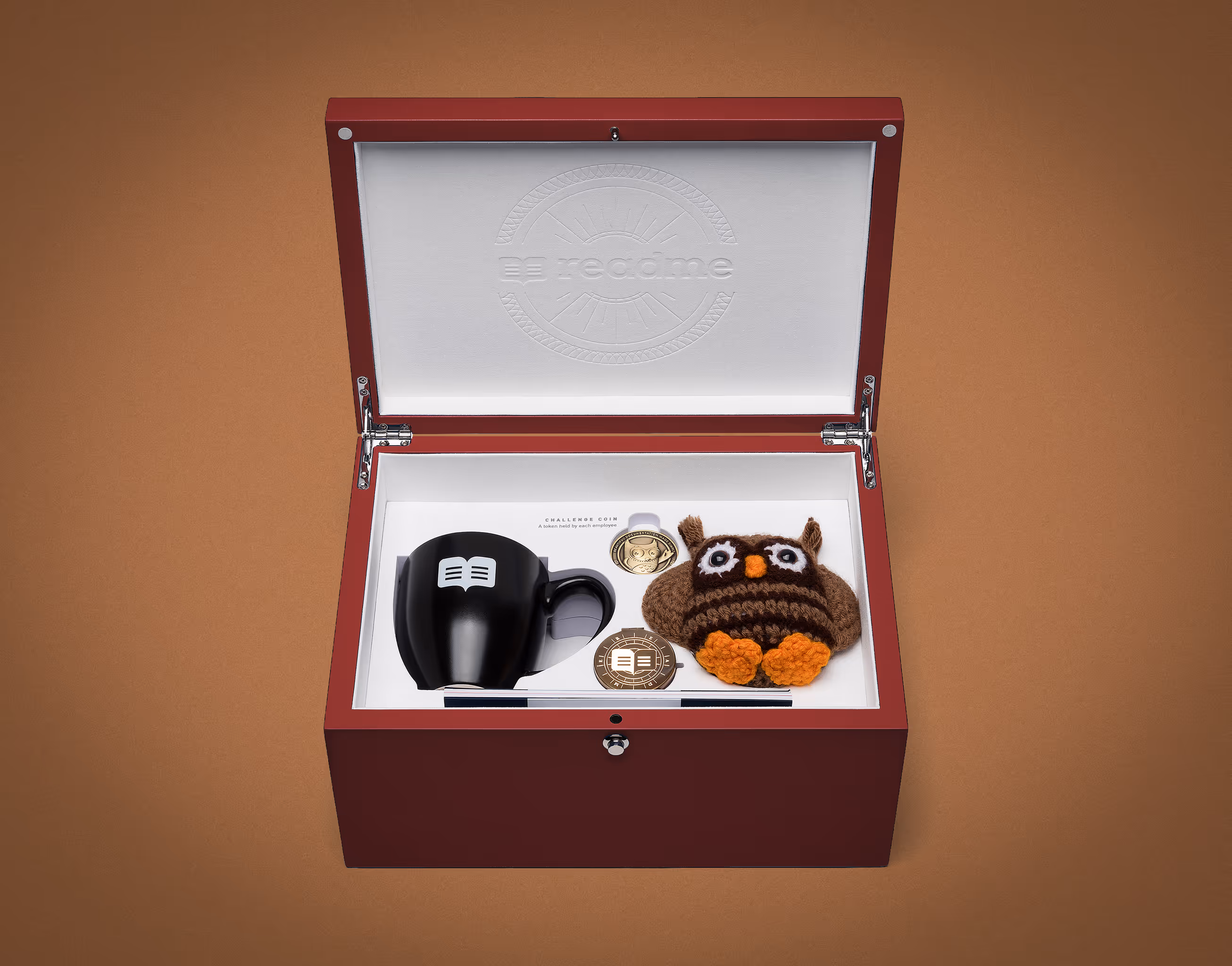 Open wooden Readme new hire box with the brand's plushie, cup, compass and coin.