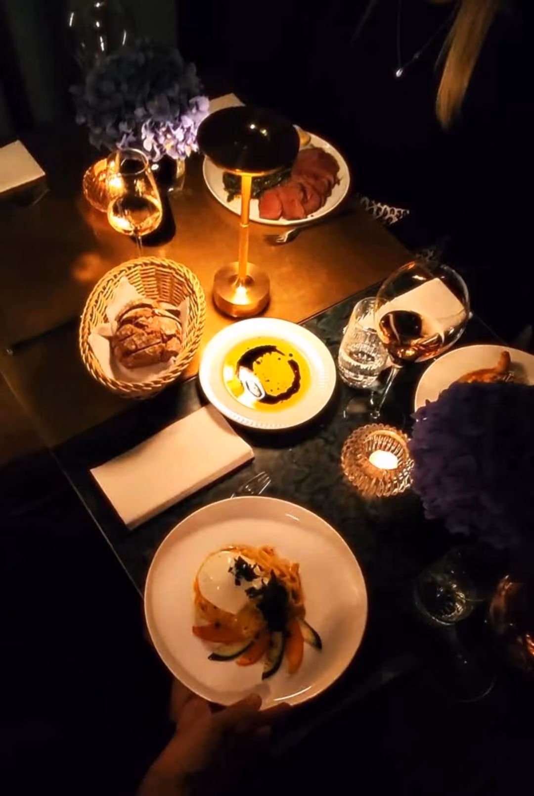 Romantisch gedeckter Tisch mit Pasta, Brot, Olivenöl, Wein und Kerzenlicht.