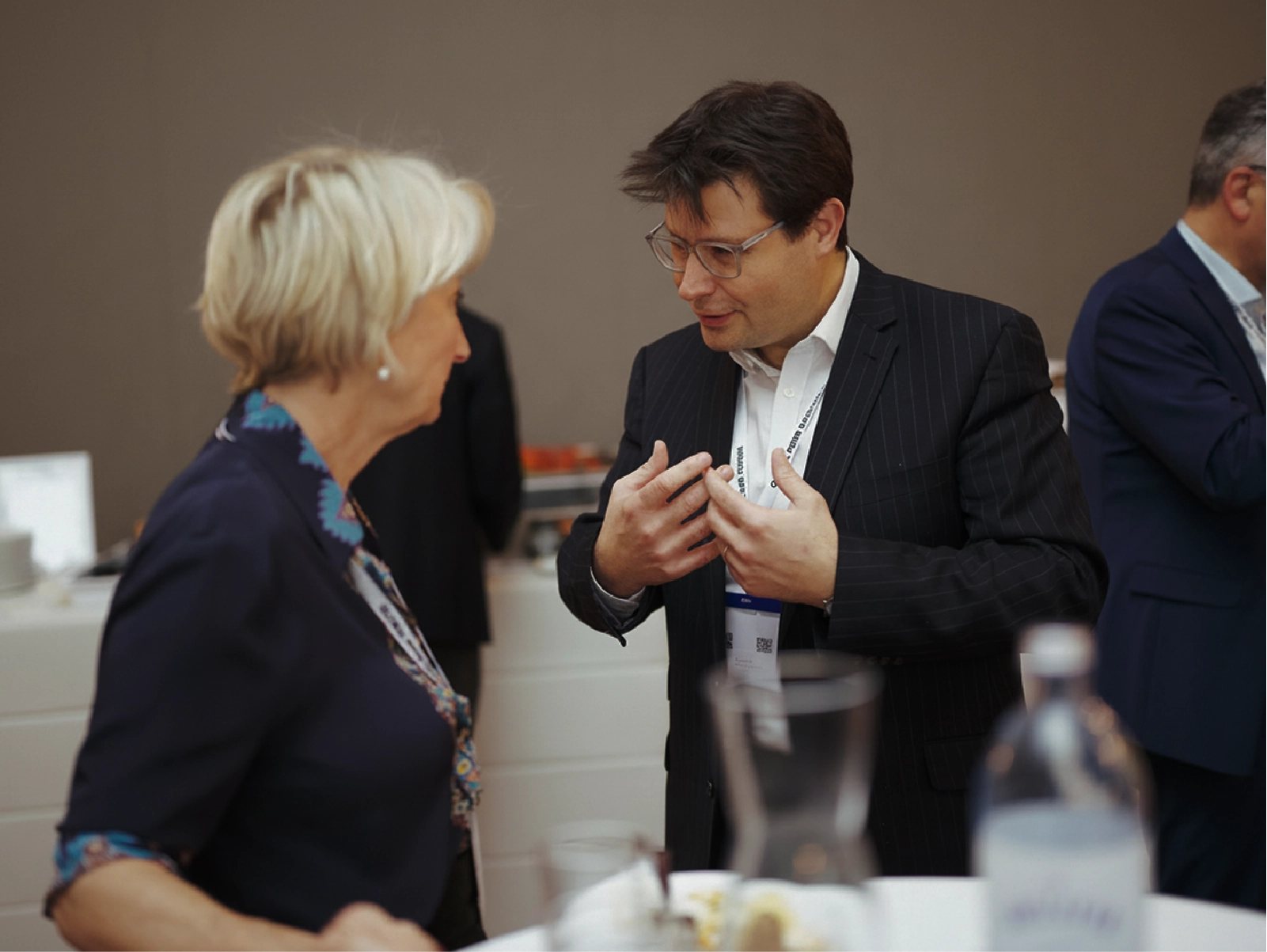 Man and woman in business attire engaged in conversation at a networking event with a table in foreground.