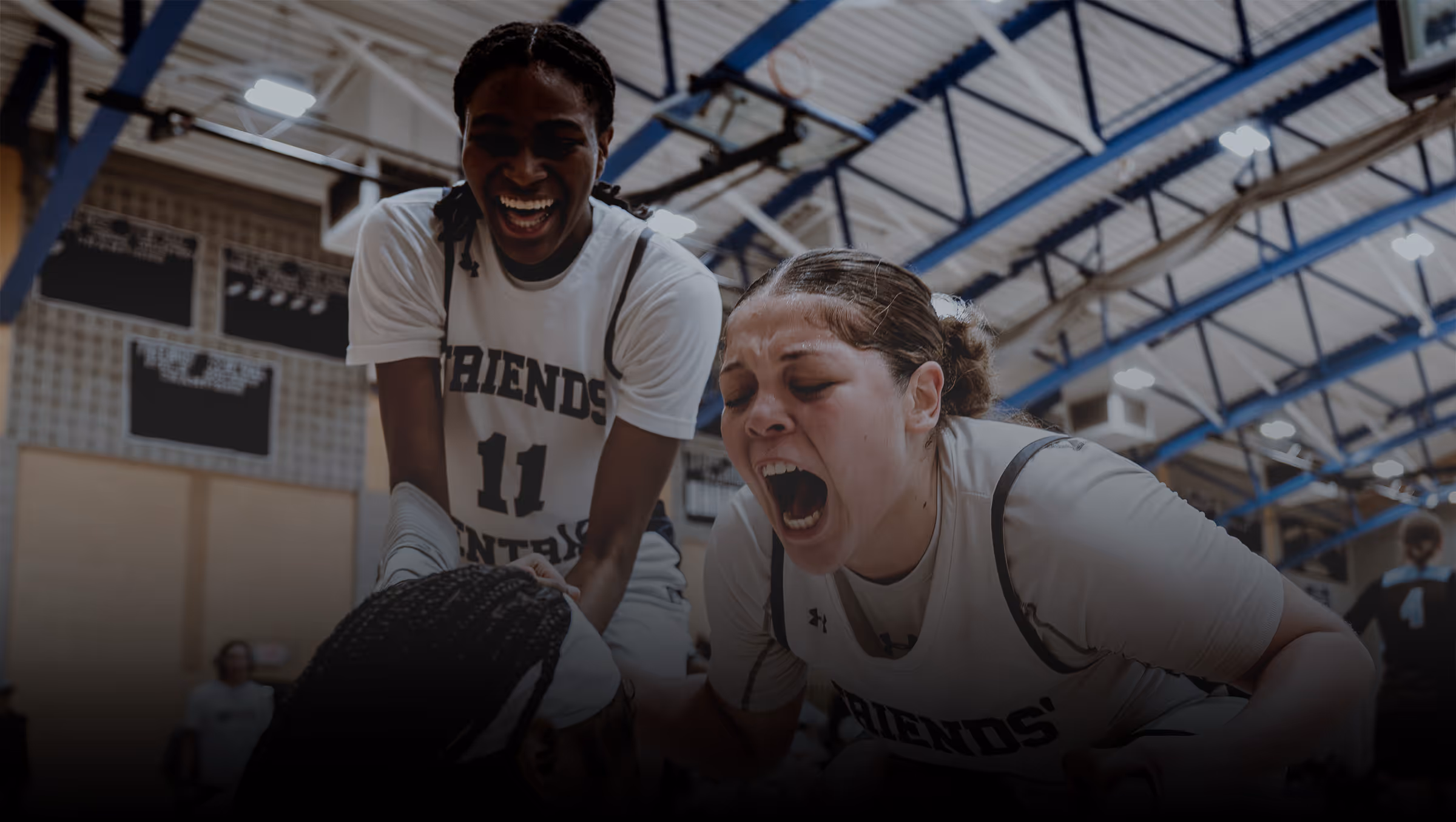 Two female basketball players celebrating intensely during a game in a gymnasium.