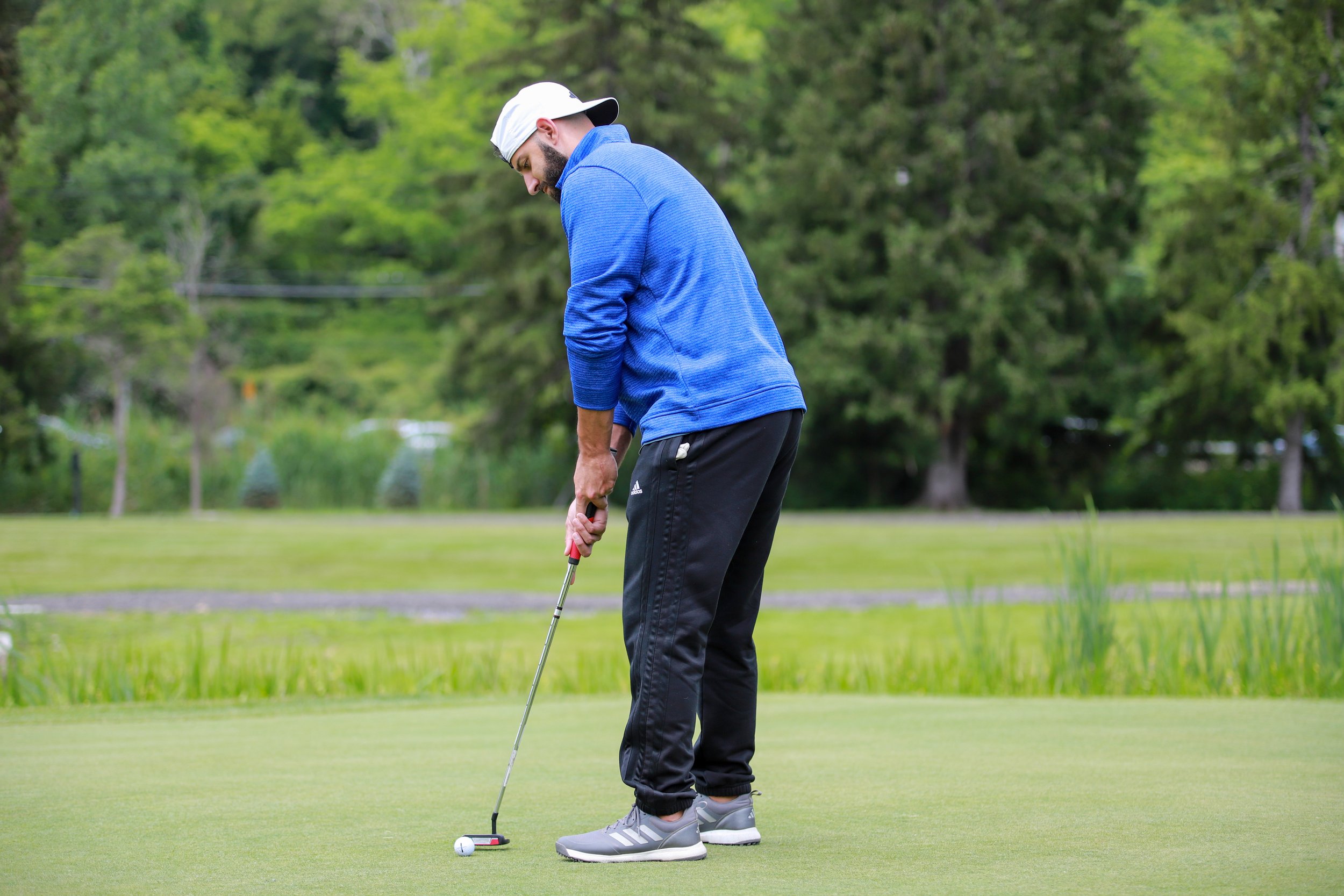 Man in a blue jacket and white cap putting a golf ball on a green golf course.