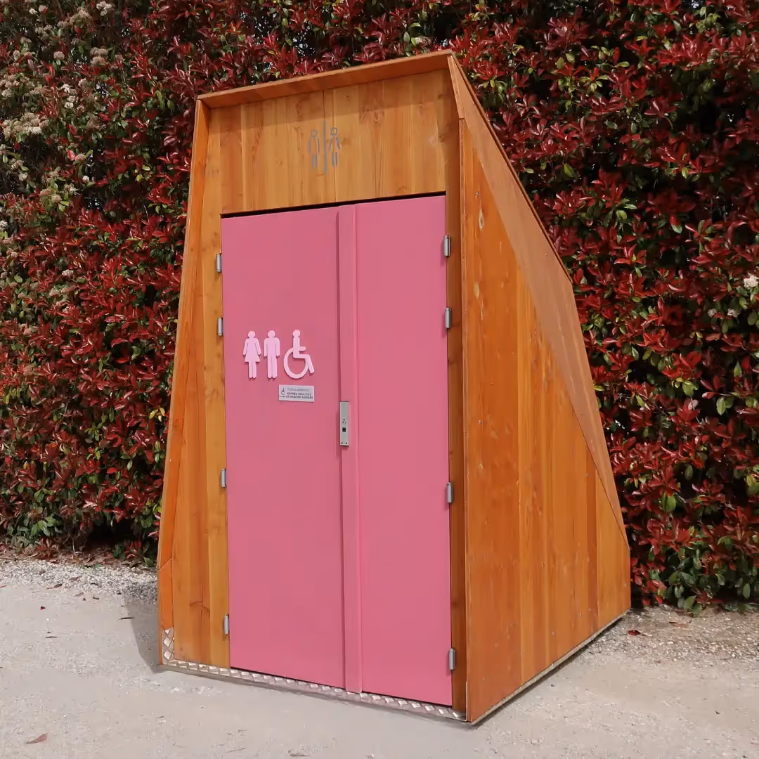 Femme qui secoue un fumigène rose devant une cabine de toilette sèche PMR avec une porte rose