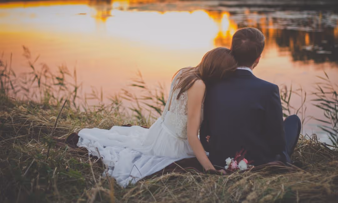 Couple de mariés assis au bord d'un lac, le soleil couchant