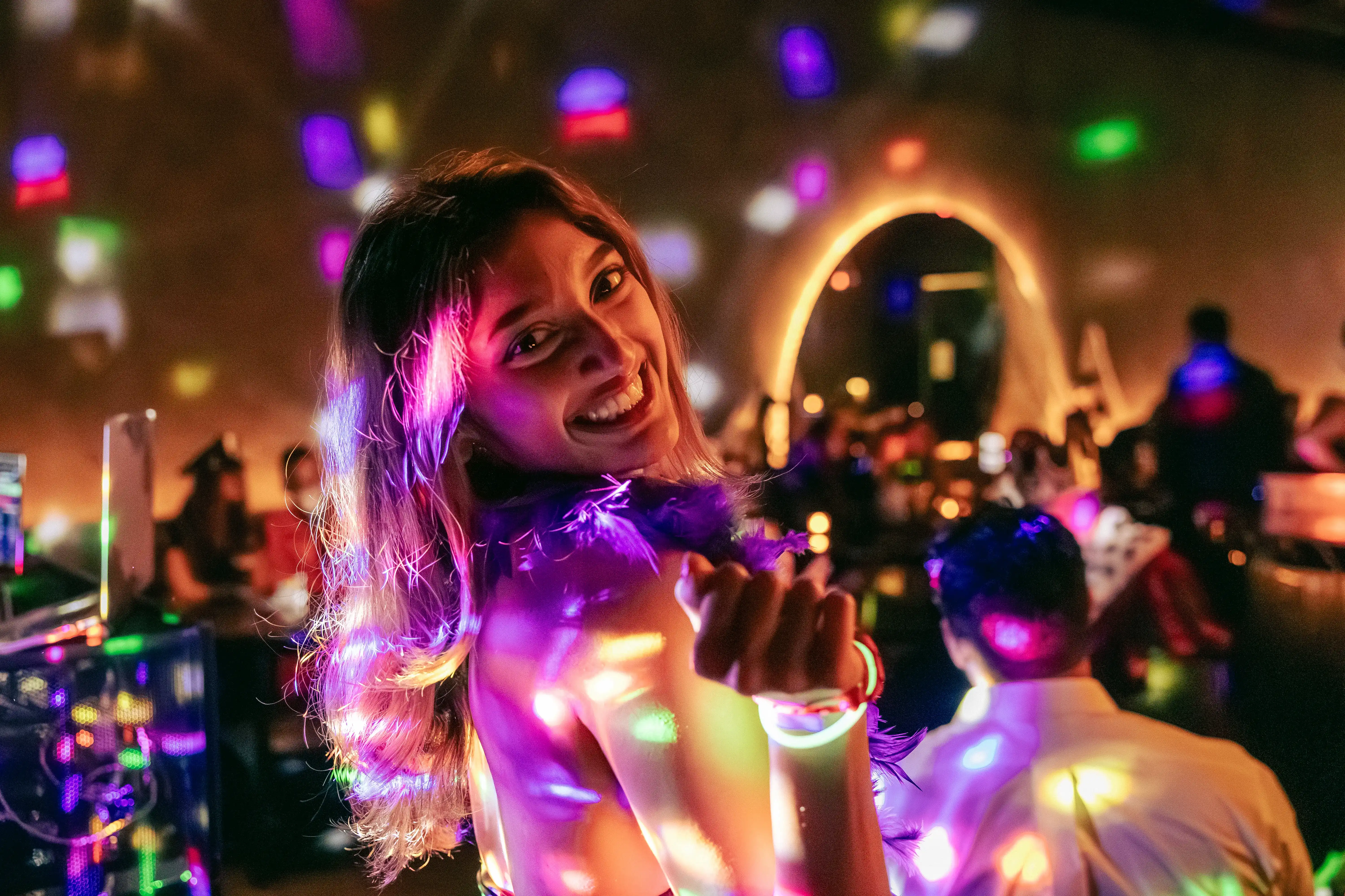 Smiling woman with long hair dancing under colorful disco lights in a lively party setting.