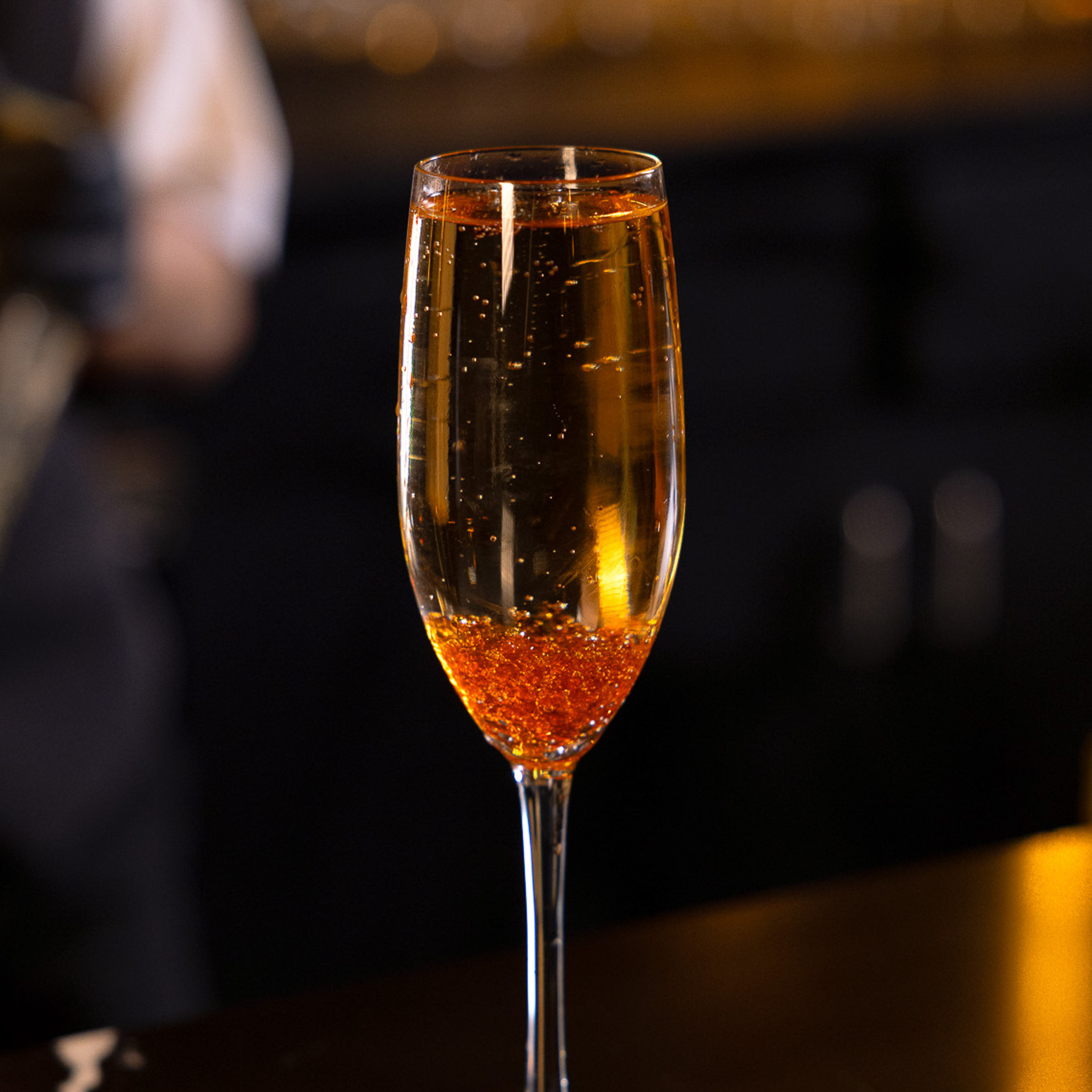 Flute glass filled with a sparkling amber cocktail with bubbles rising inside.