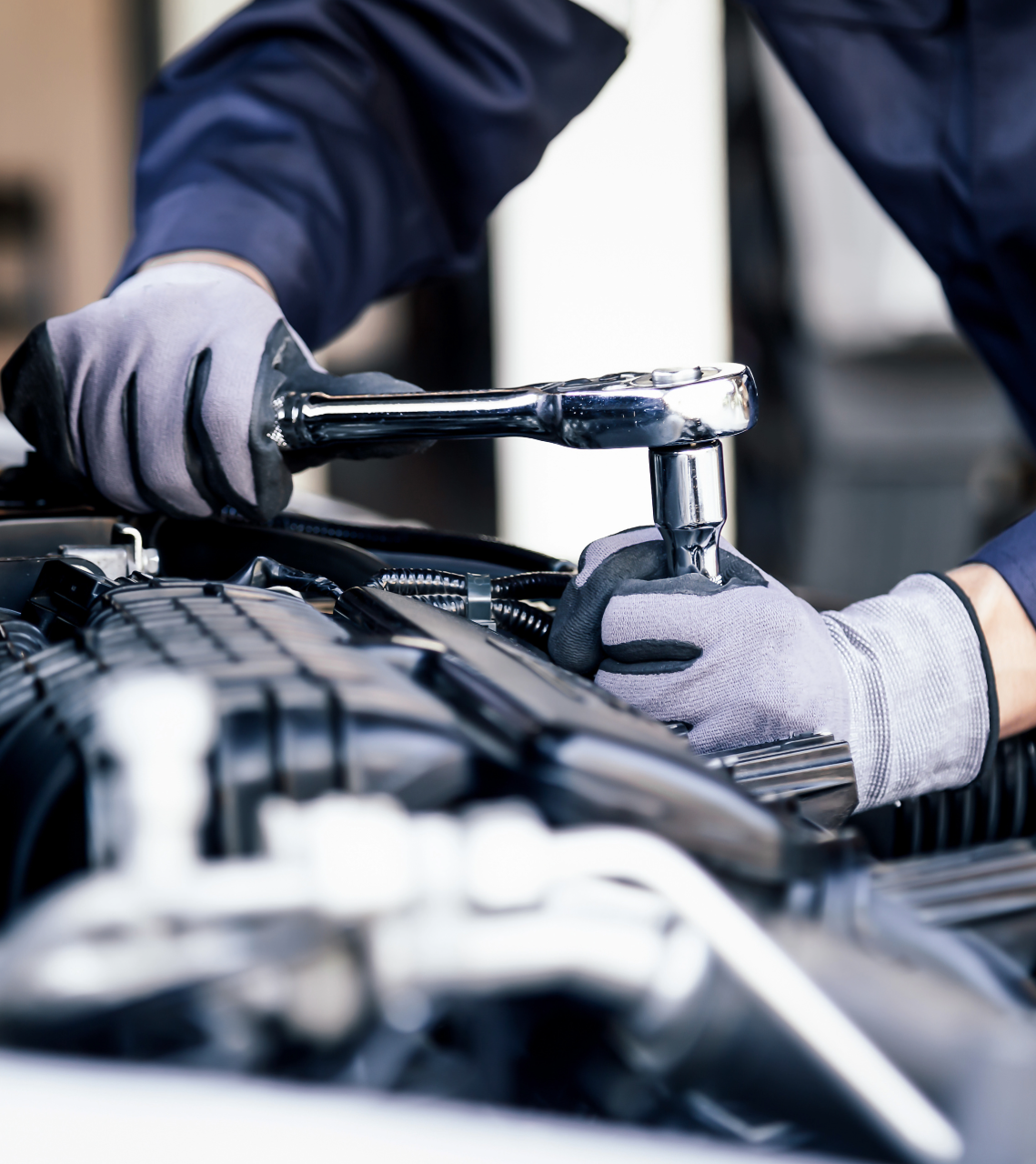 Mechanic wearing gloves using a ratchet wrench to work on a car engine.