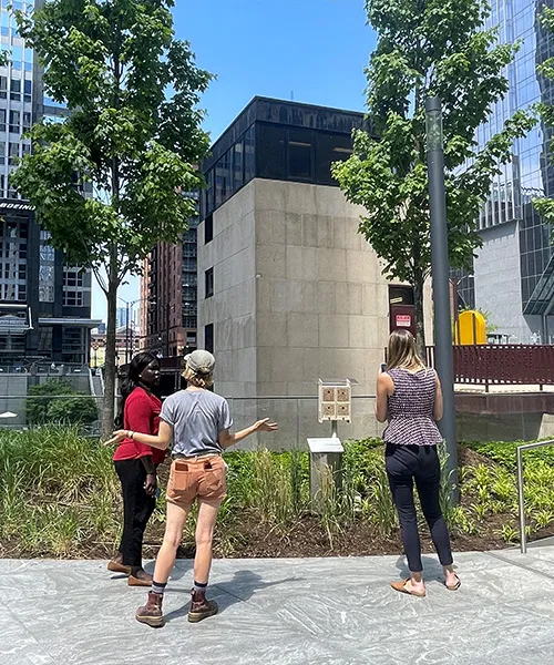 Une apicultrice d'Alvéole s'adresse à deux femmes qui observent une BeeHome sur une terrasse.