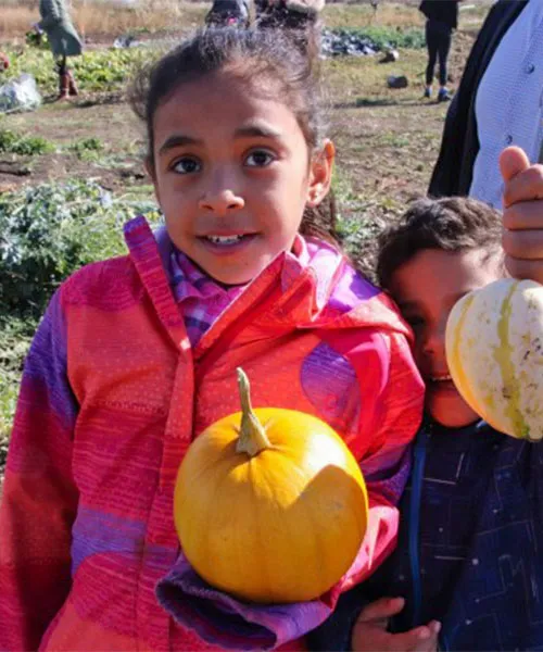 A child holding a pumpkin. community farming initiatives