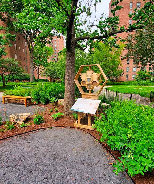 Un hôtel à abeilles en bois avec un panneau éducatif sur la façade se trouve dans un jardin paysager. importance des pollinisateurs