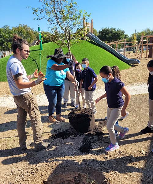 A group of children and two adults plant a tree. tree planting initiatives