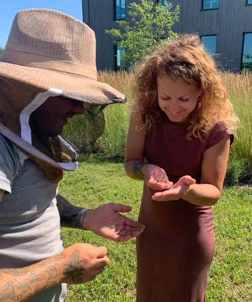A woman holds a honey bee in her hand as beekeeper watches. ways to protect pollinators