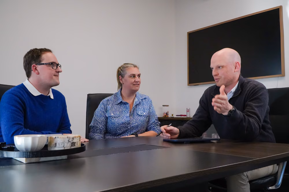 Jake Harris leading an in-person business and mindset strategy meeting with two clients in an office.