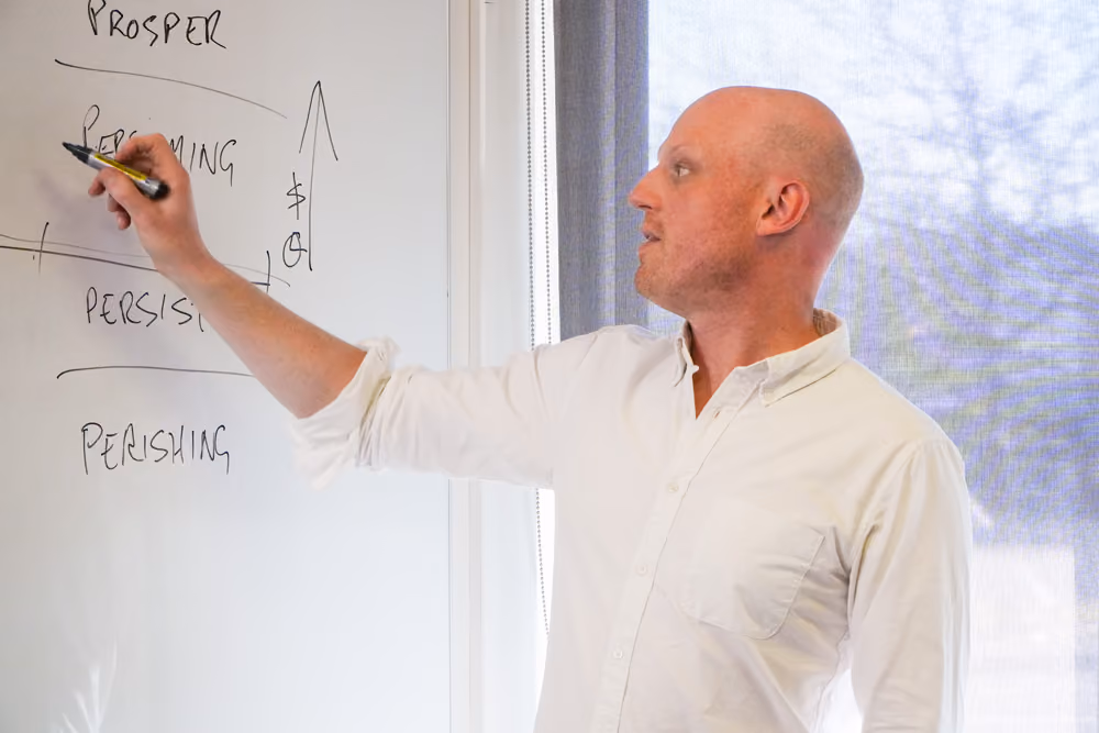 Jake Harris, Melbourne business and mindset coach, writing a growth diagram on a whiteboard during a strategic coaching session.