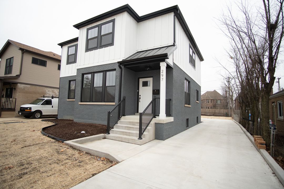 Modern two-story new construction home with dark gray brick on the first level, white vertical siding on the second level, and black trim details.