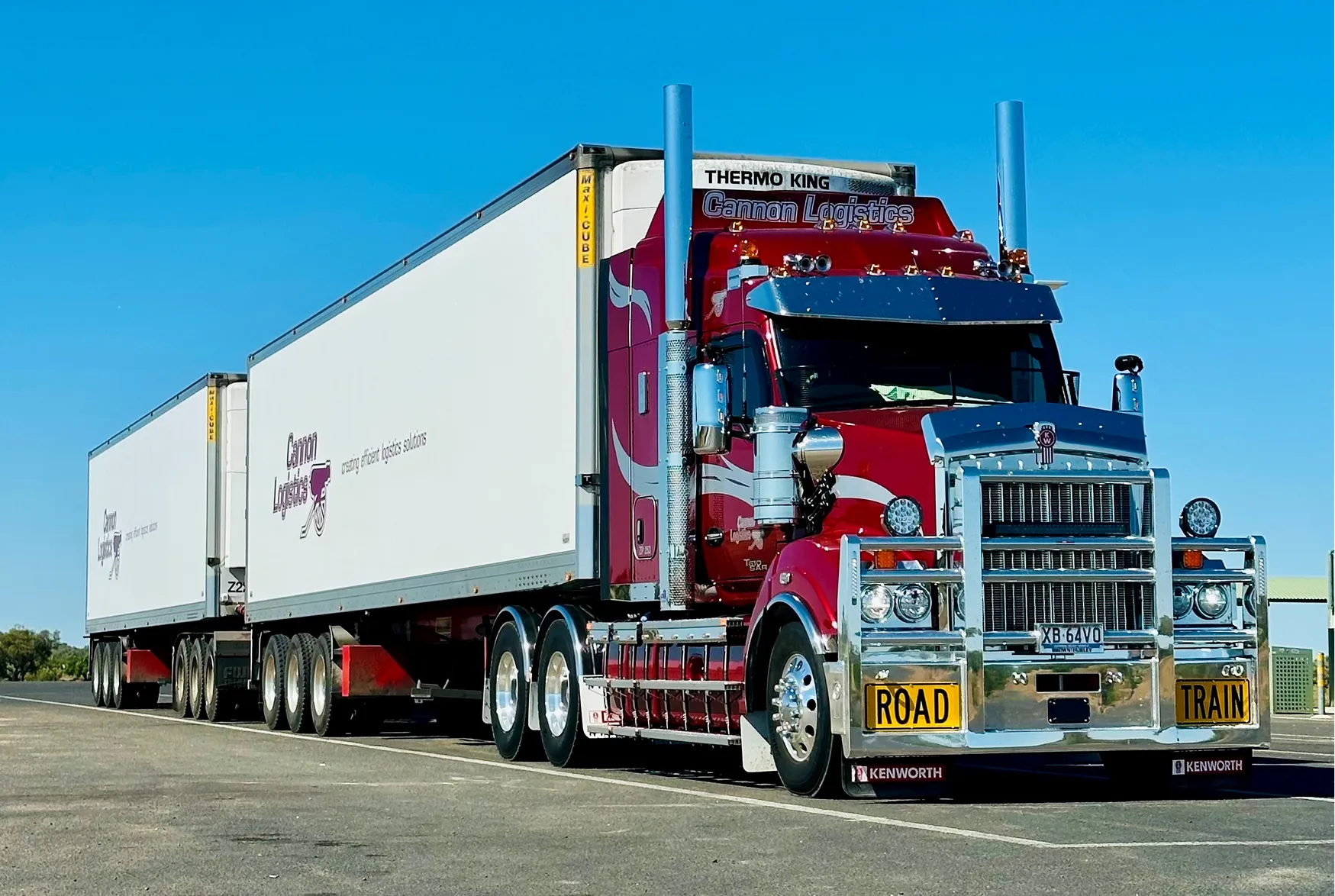Red Kenworth road train truck with two white Cannon Logistics trailers on a clear day.