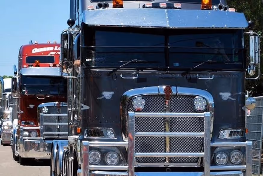 Front view of a black semi-truck with chrome grill and another red semi-truck behind it on a road.
