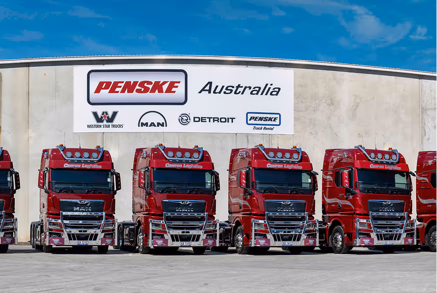 Row of red Canon Logistics trucks parked in front of a building with a large Penske Australia sign.