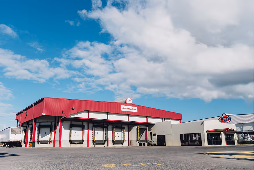Large warehouse building with red roof labeled Cannon Logistics under a partly cloudy blue sky.