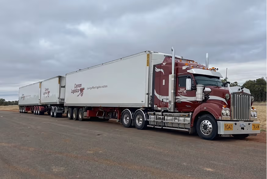 Large maroon and white Cannon Logistics road train truck parked on a road with an overcast sky.