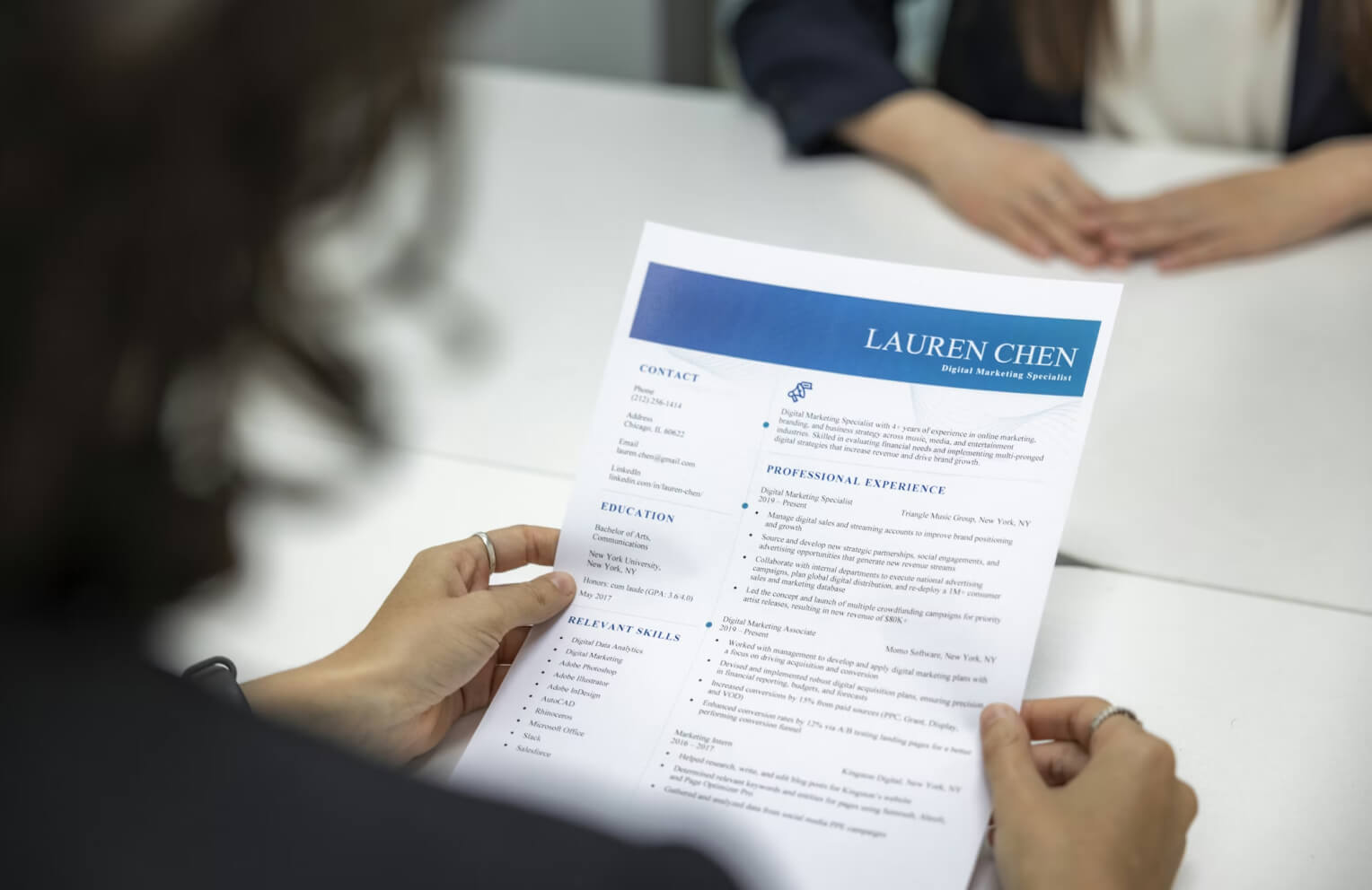 Person holding a resume of Lauren Chen, Digital Marketing Specialist, during a job interview at a white table.