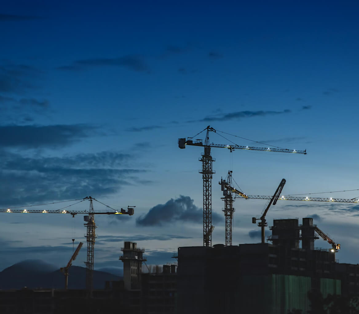 Construction cranes and building structures silhouetted against a twilight sky with scattered clouds.