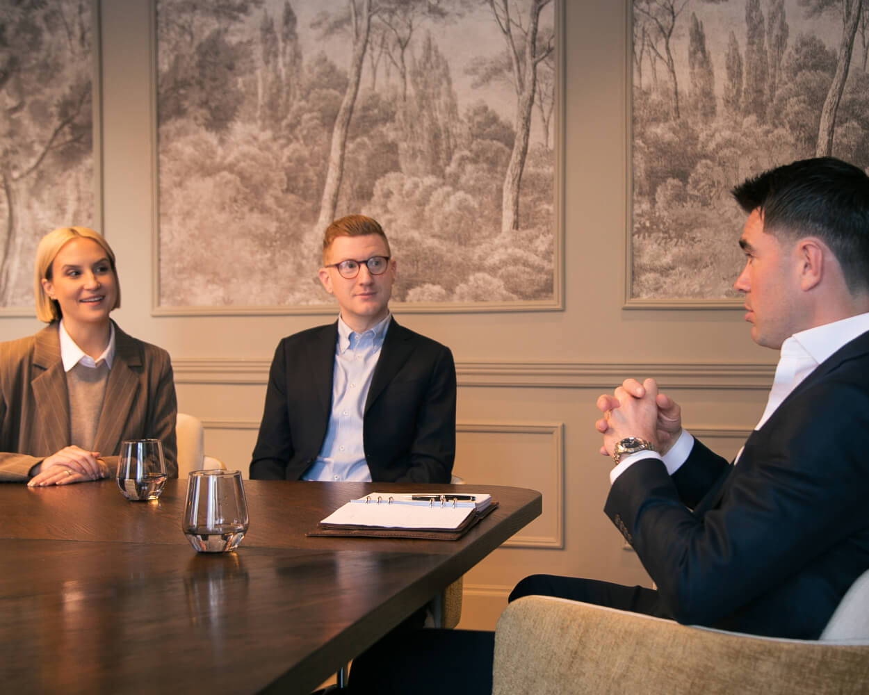 Three business professionals having a meeting at a wooden table in a formal setting.