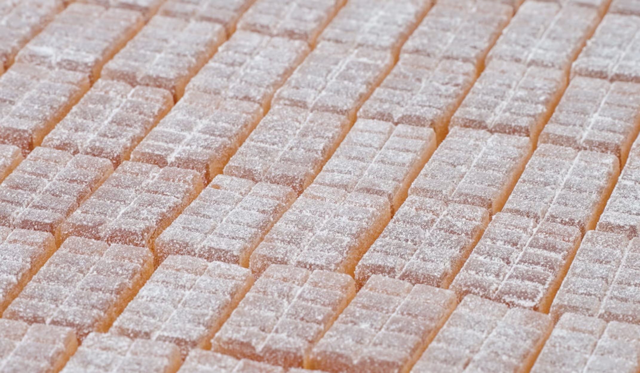 Rows of rectangular peach-colored gummy candies dusted with sugar.