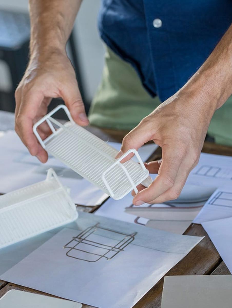OA Brand image. Person holding a white architectural model over a table with design sketches.