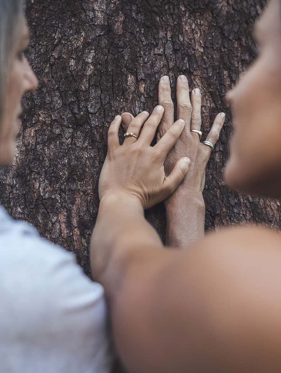 Gwinganna Brand image. Two people with wedding rings touching their hands together on tree bark.