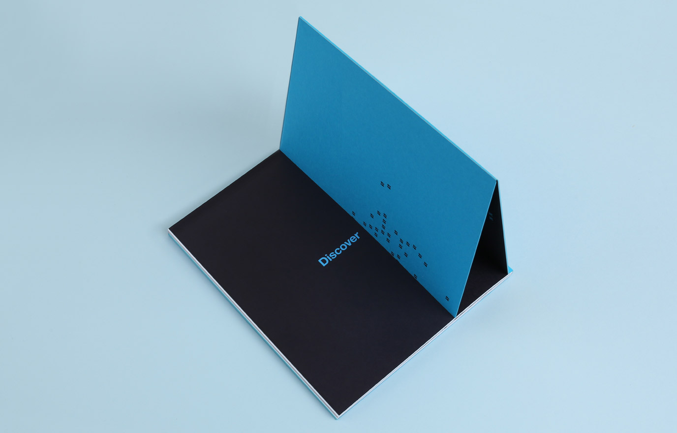 Burling borwn book. Open booklet with an inside page featuring the word 'Discover' in blue and a blue triangular folded page with small black symbols.