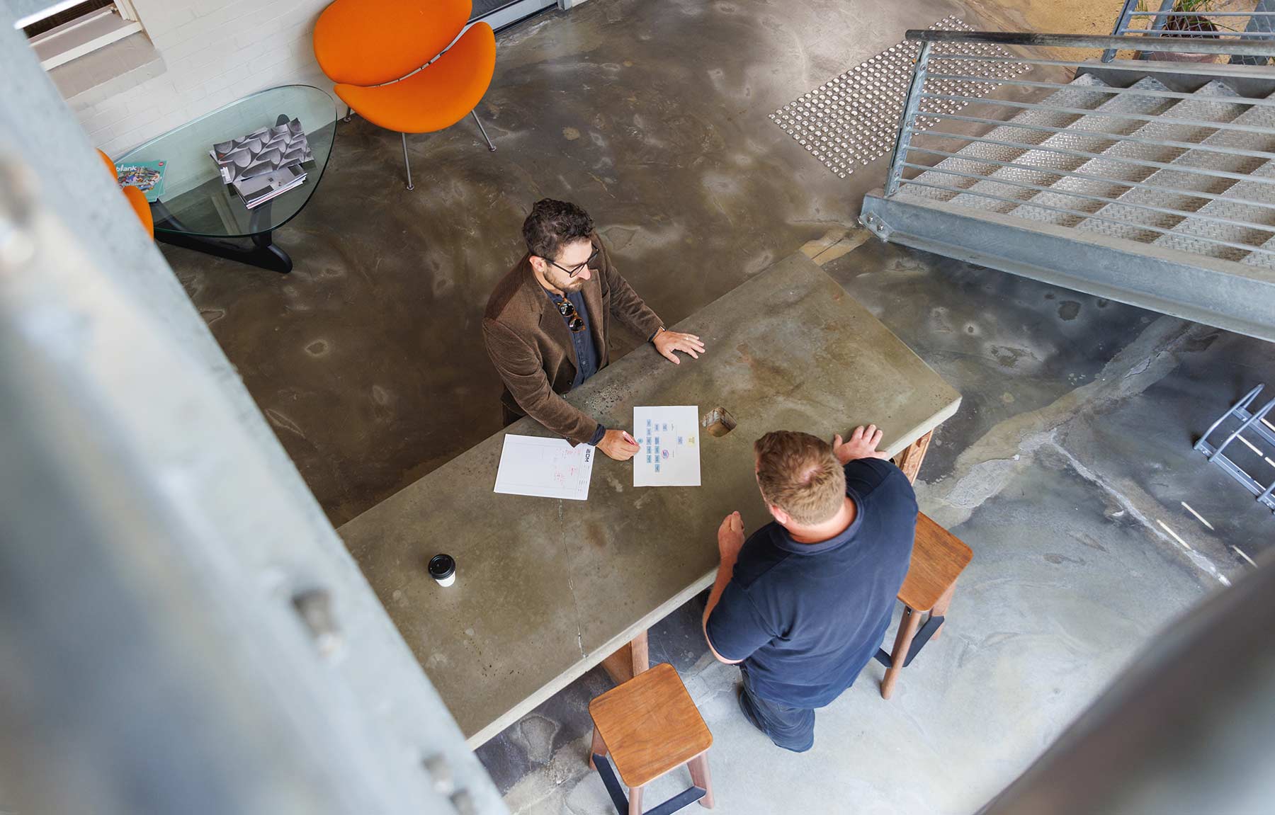 IEDM. Two men standing and discussing over papers on a concrete table in a modern industrial-style office space.