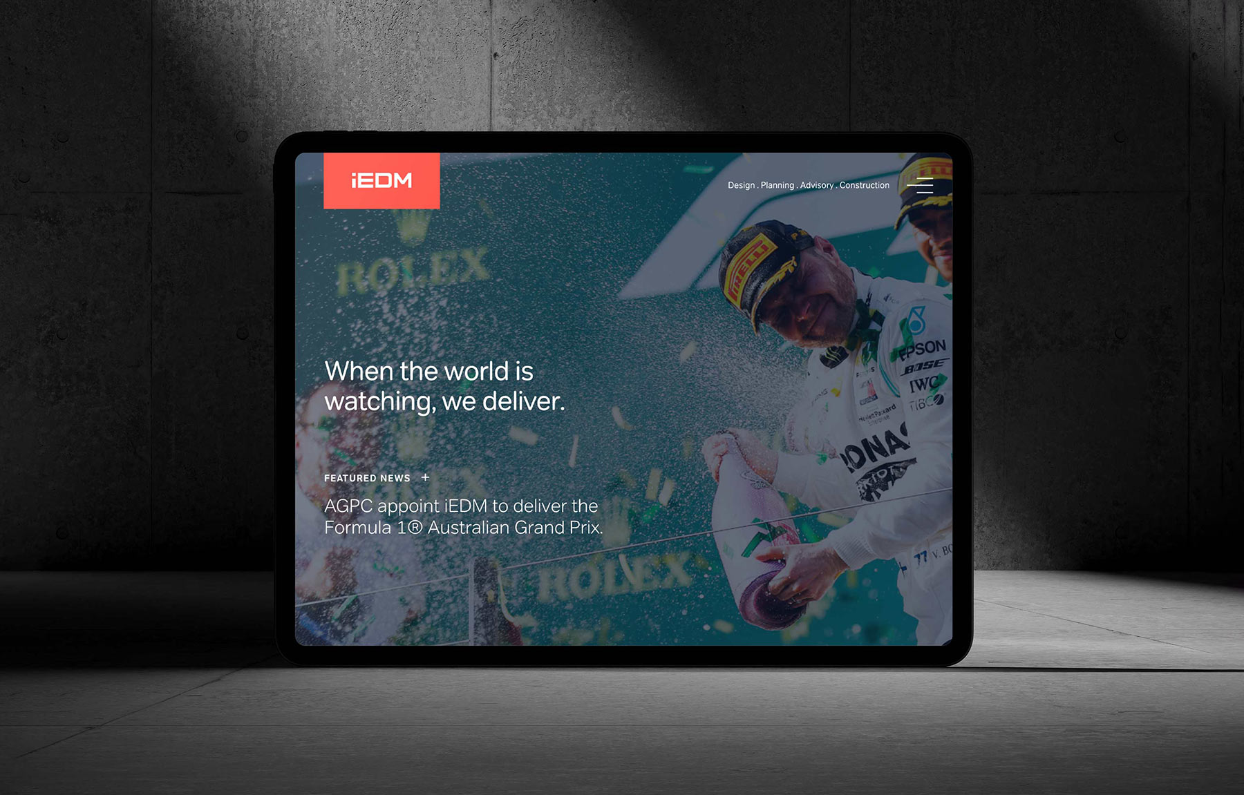 IEDM Website. Tablet screen displaying iEDM website with F1 driver celebrating spraying champagne at Australian Grand Prix.