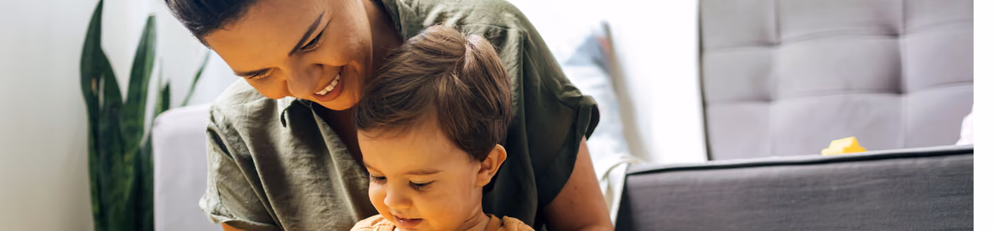 Smiling woman playing with a toddler in a cozy living room setting.