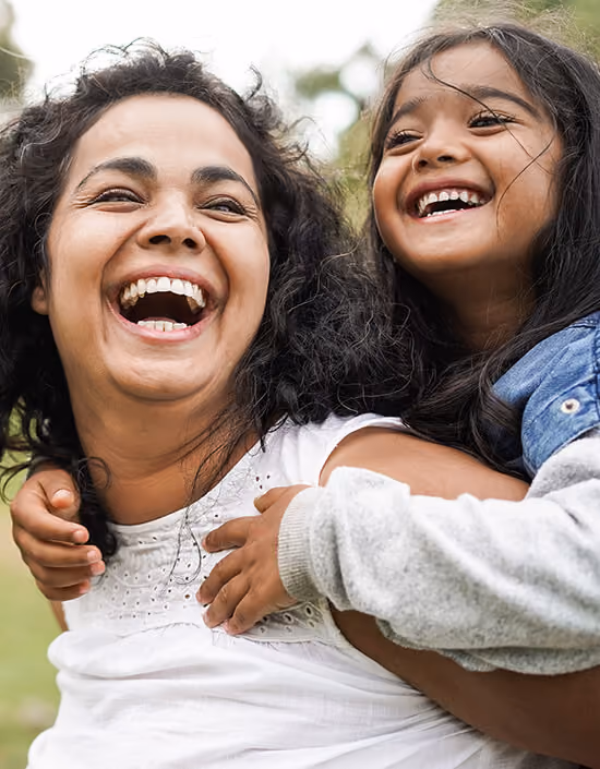 Smiling woman carrying a happy child on her back outdoors.