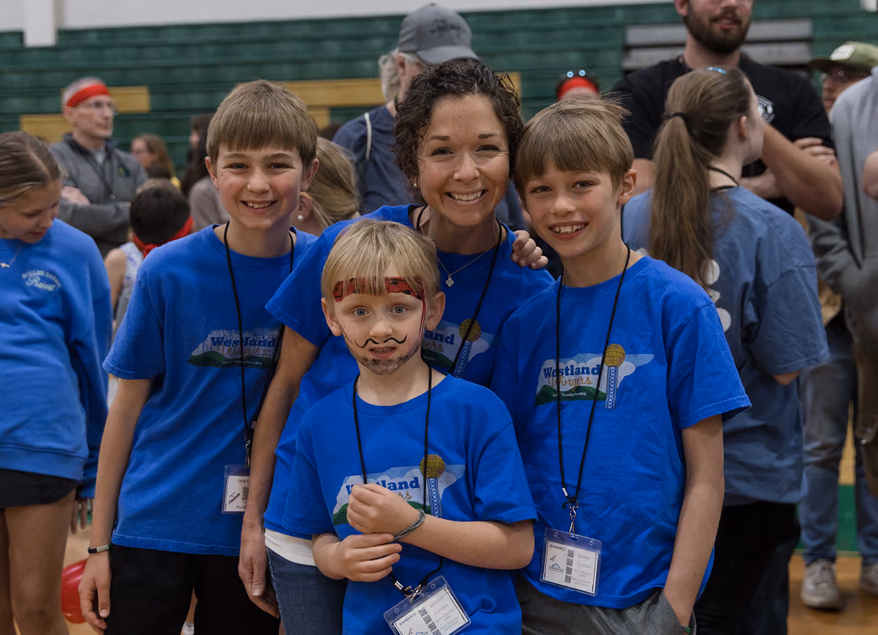 Smiling woman with three boys in blue Westland Cougars shirts at an indoor event.