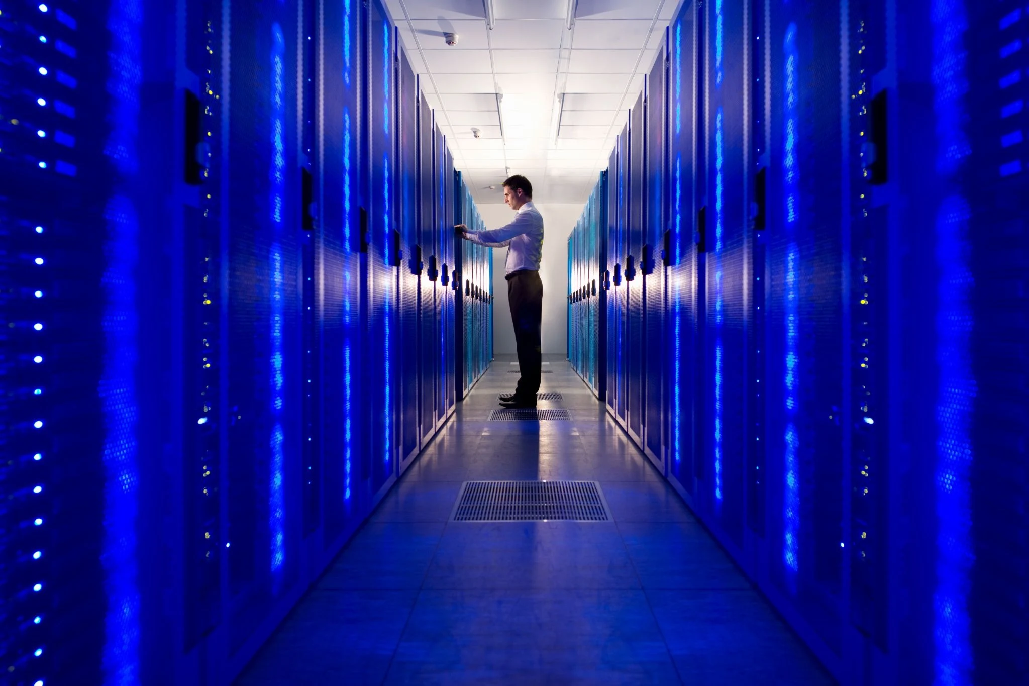 IT professional standing in modern server room corridor with rows of blue-lit server racks in a data center