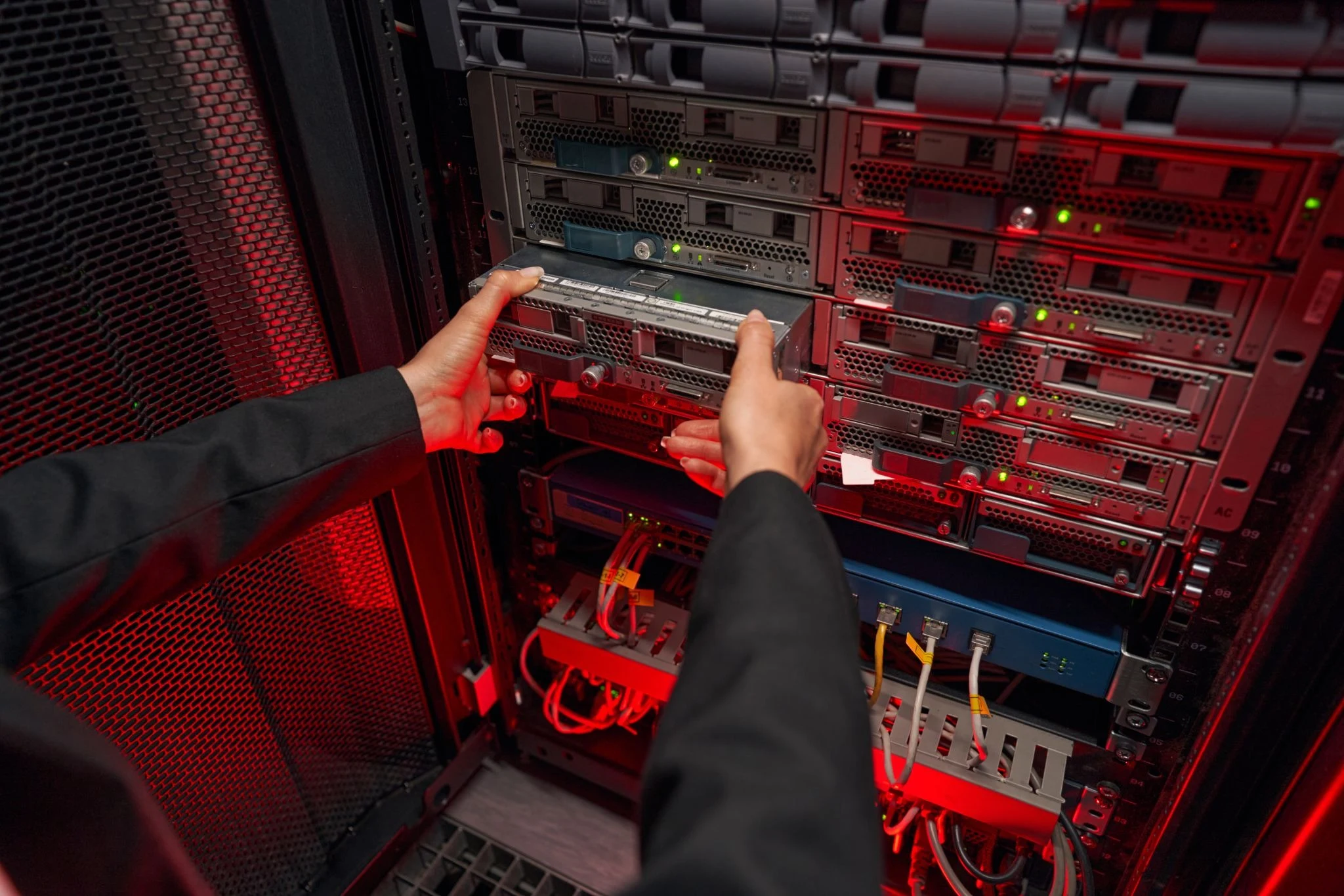 IT technician replacing hard drive in enterprise server storage system rack in data center with red ambient lighting