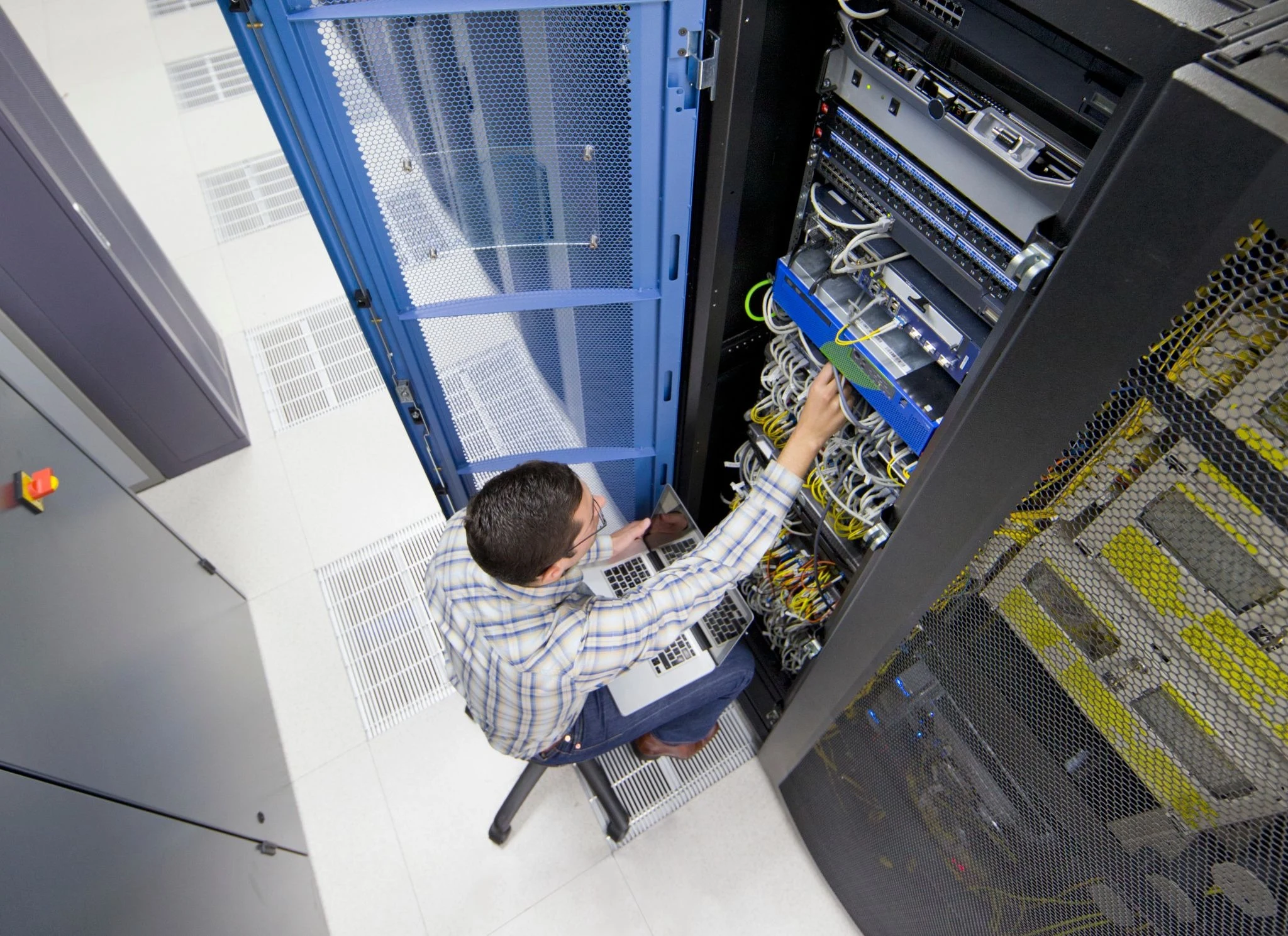 Top angle view of IT technician working on server rack with laptop in data center for network maintenance