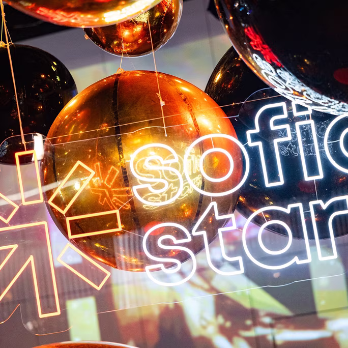 Shiny gold and black balloons with illuminated decorative text reading 'sofi star' in white neon lights.
