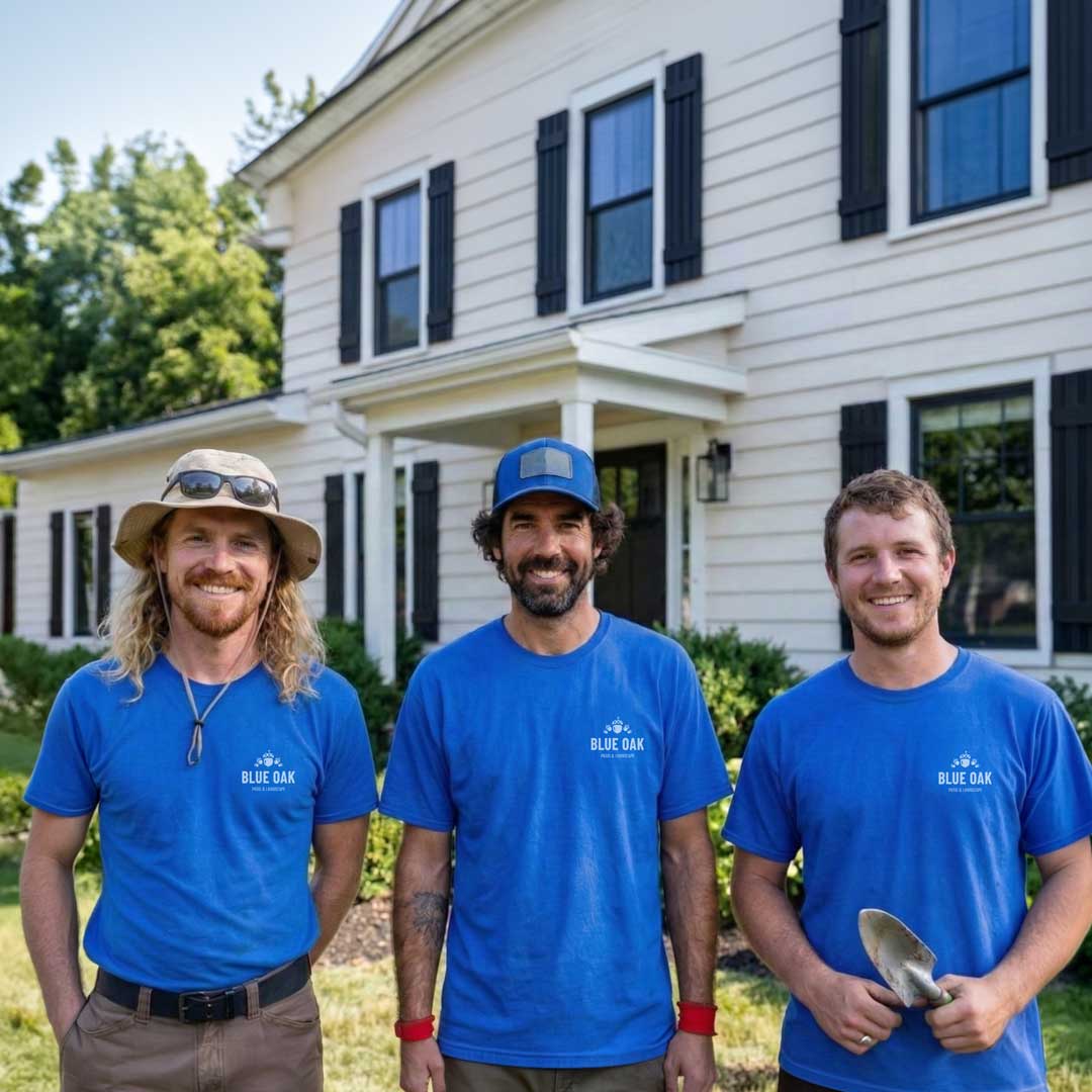 Three men wearing blue Blue Oak Pest & Landscape t-shirts standing outside a white house with black shutters.