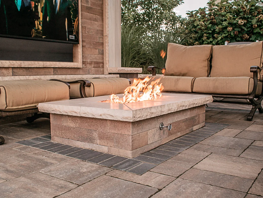 Outdoor seating area with cushioned benches around a rectangular stone fire pit with flames.