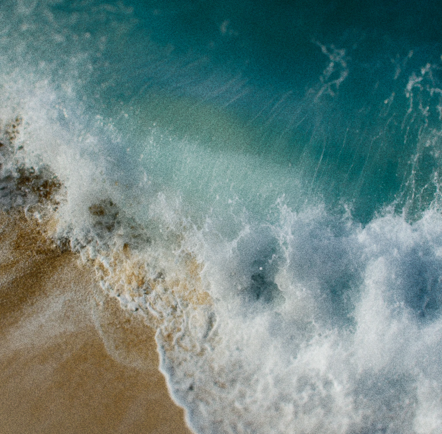 Aerial view of ocean waves crashing onto a sandy shore with white sea foam.