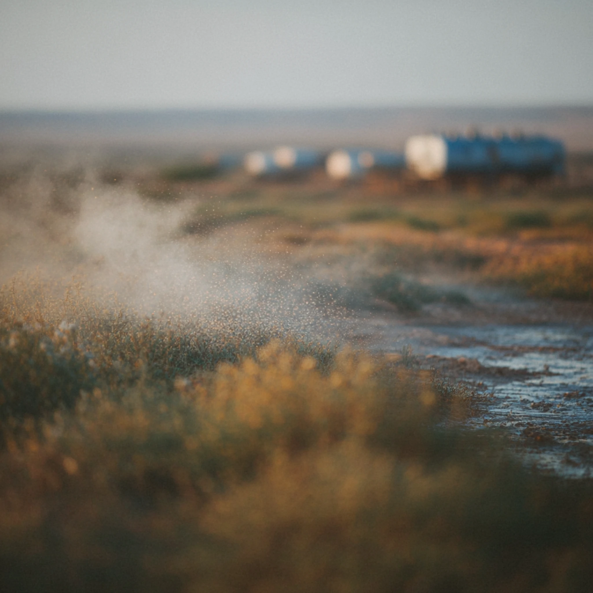 A dirt path through grass with water droplets or mist in the air and blue blurred trailers in the background.